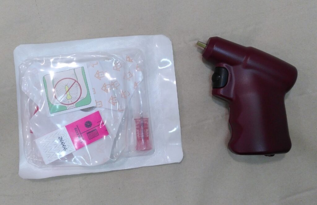 Equipament necessari per a la inserció d'una agulla intraòssia EZ-IO. A la dreta de la imatge hi veiem la pistola perforadora, un estri de color granat, amb una empunyadura i un gatell de color negre. A la part superior d'aquesta empunyadura i en un angle d'uns 30º sobresurt lleugerament l'adaptador per a connectar-hi l'agulla a inserir. A l'esquerra de la imatge hi ha l'envàs de plàstic d'una agulla pediàtrica (rosa). Dins aquest envàs hi podem veure l'agulla, l'apòsit de fixació, una banda identificativa. També s'hi veu un dibuix d'un tòrax humà amb un senyal de prohibició sobre l'estèrnum (per indicar que no és un dispositiu esternal).