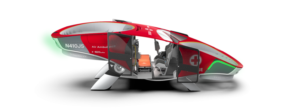 Disseny d'una ambulància voladora futurista vista de perfil. De forma semblant a un vehicle monovolum, pintada de color vermell i logotipada com a ambulància. Porta dos grans rotors en els extrems, el vehicle es suporta al terra amb una mena de potes. Al centre del vehicle, uns portes corredisses obertes donen accés a l'habitacle. En aquest habitacle hi ha dos seients, un mirant a l'exterior en el sentit de la marxa i un altre mirant a la llitera que està posada perpendicular al sentit de la marxa